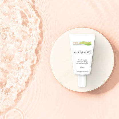 Eine Tube Celyoung Anti Rot plus LSF 50 Fluid ist auf einer beigen, runden Plattform neben plätscherndem Wasser abgebildet, mit sanfter rosa Beleuchtung im Hintergrund.